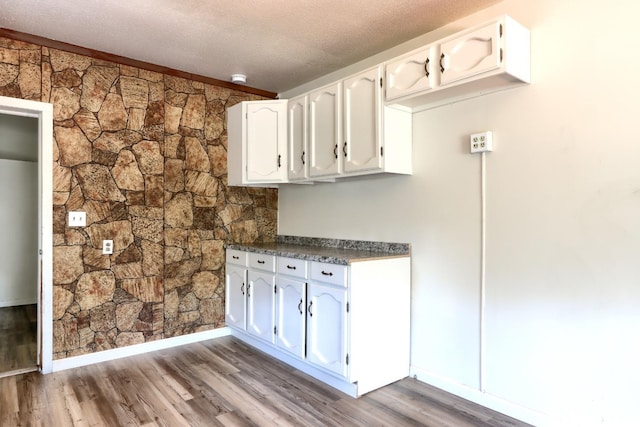 interior space featuring wood finished floors, dark countertops, white cabinetry, a textured ceiling, and baseboards