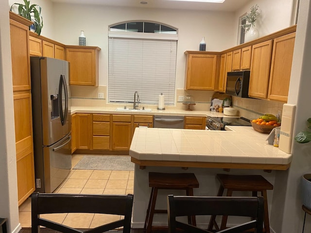 kitchen featuring a sink, a peninsula, tile countertops, backsplash, and appliances with stainless steel finishes