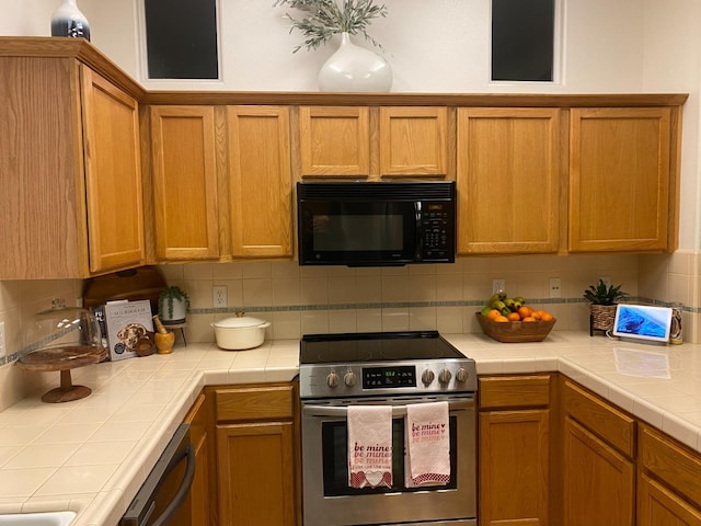 kitchen featuring brown cabinetry, stainless steel appliances, tasteful backsplash, and tile countertops