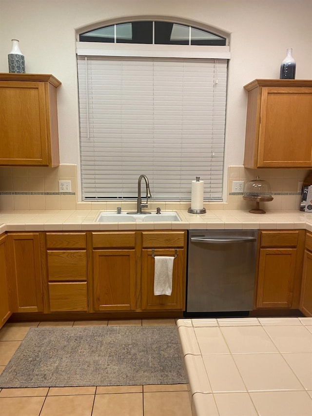kitchen featuring a sink, stainless steel dishwasher, backsplash, and tile counters