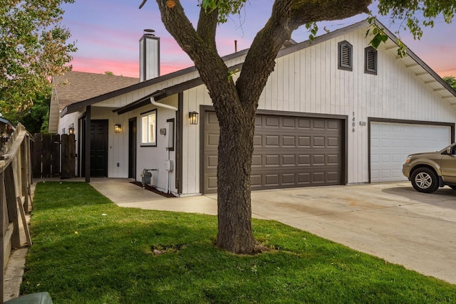 view of front of home featuring a chimney, fence, board and batten siding, a yard, and driveway