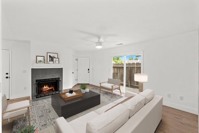 living area featuring wood finished floors, visible vents, a fireplace, ceiling fan, and baseboards