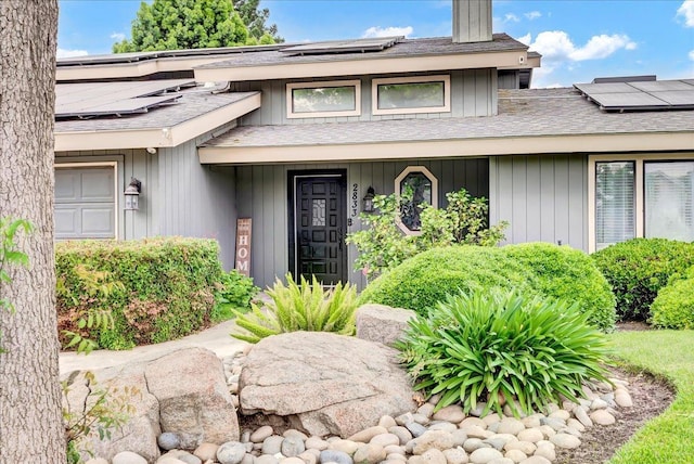 property entrance featuring a shingled roof, a porch, and solar panels