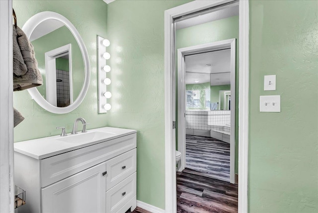 bathroom with toilet, wood finished floors, baseboards, a textured wall, and vanity