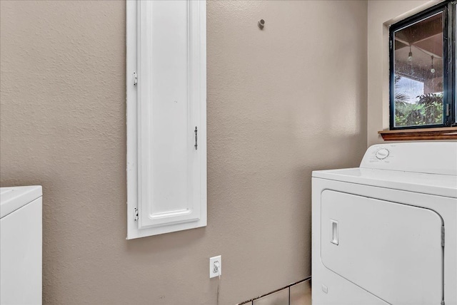 clothes washing area with laundry area, a textured wall, and washer and clothes dryer