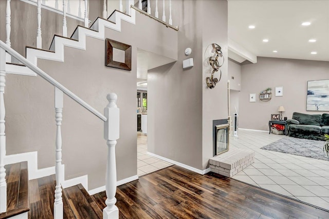 stairs with recessed lighting, baseboards, high vaulted ceiling, wood finished floors, and a fireplace