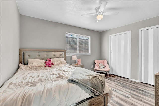 bedroom featuring baseboards, a ceiling fan, multiple closets, and wood finished floors