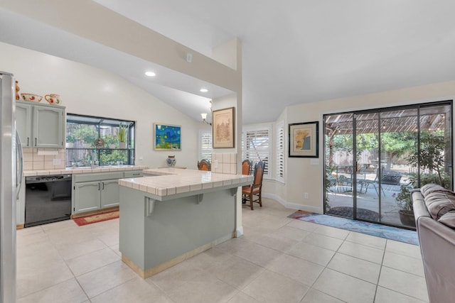 kitchen featuring dishwasher, light tile patterned flooring, vaulted ceiling, backsplash, and tile counters