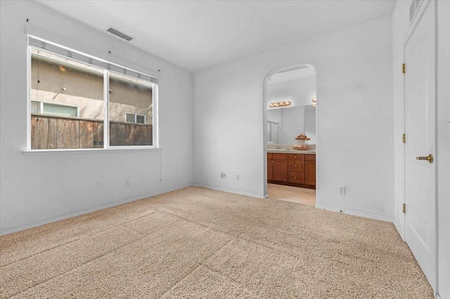 unfurnished bedroom with light carpet, ensuite bath, and visible vents