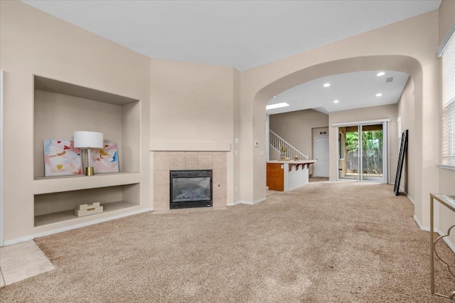 unfurnished living room with stairway, carpet floors, arched walkways, and a tiled fireplace