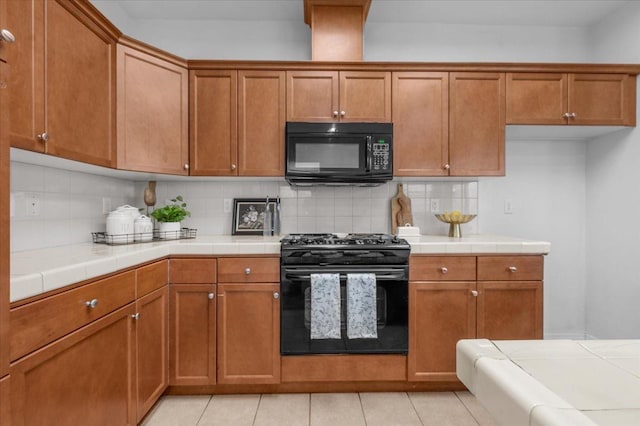 kitchen featuring brown cabinetry, tile counters, black appliances, and backsplash