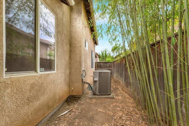 view of side of property featuring stucco siding, fence, and central AC