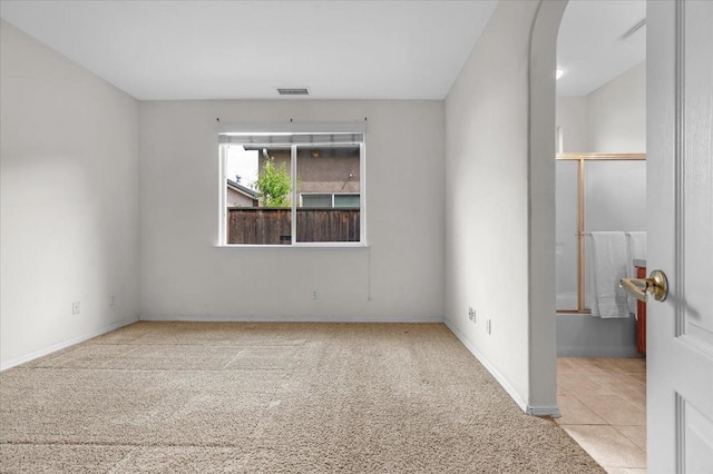 unfurnished room with light colored carpet, visible vents, baseboards, and arched walkways