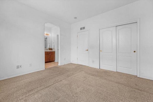 unfurnished bedroom with a closet, baseboards, visible vents, arched walkways, and light carpet