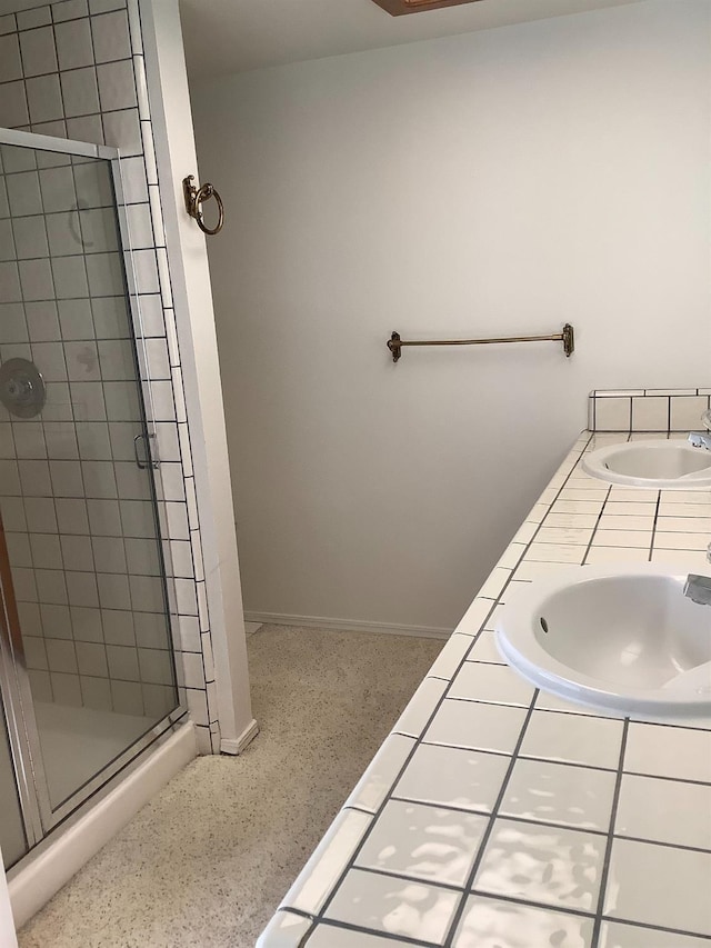 full bath with double sink, baseboards, a shower stall, and speckled floor