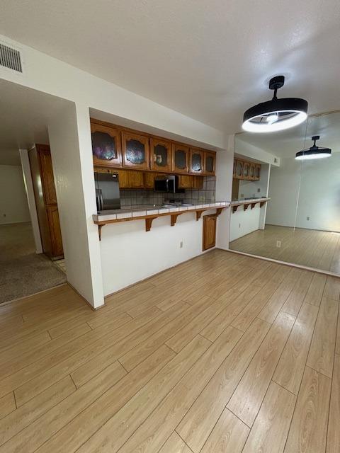 7093 N Teilman Unit 102, Fresno, CA 93711 - kitchen with stainless steel microwave, a kitchen bar, light wood-type flooring, and glass insert cabinets