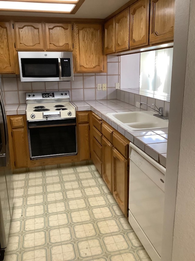 kitchen featuring white dishwasher, light floors, a sink, stainless steel microwave, and electric range