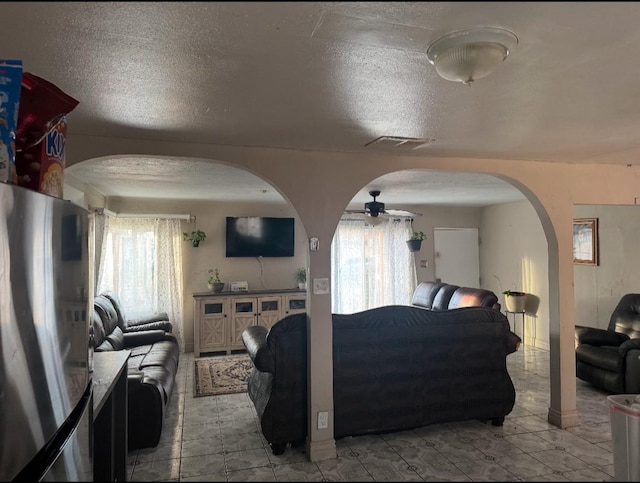 living room featuring plenty of natural light, visible vents, arched walkways, and a textured ceiling