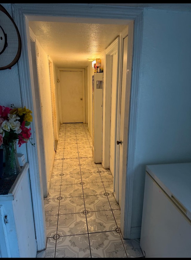 hall with a textured ceiling and light tile patterned floors