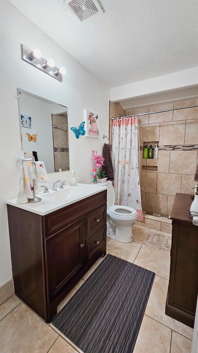 bathroom with toilet, tiled shower, tile patterned floors, visible vents, and vanity