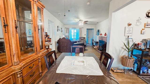 dining space with wood finished floors, a fireplace, and ceiling fan