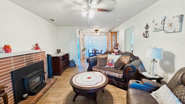 living room with ceiling fan, a wood stove, light wood finished floors, and visible vents