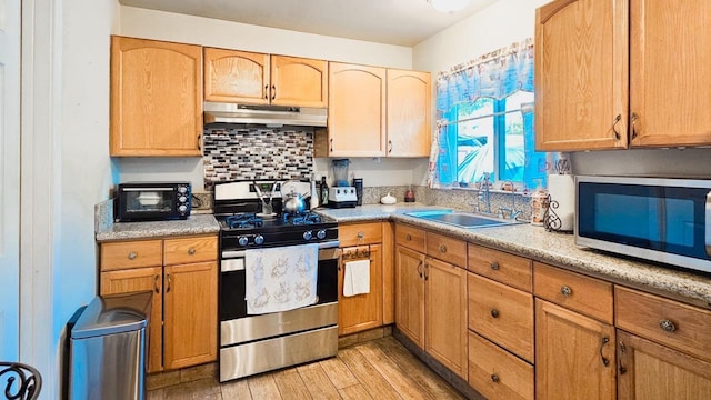 kitchen with a sink, stainless steel appliances, under cabinet range hood, light wood finished floors, and decorative backsplash