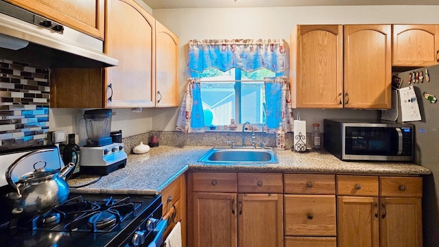 kitchen with stainless steel microwave, a sink, under cabinet range hood, light countertops, and range with gas stovetop