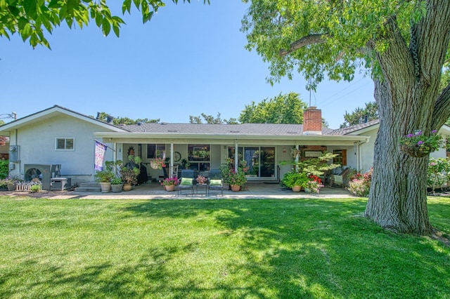 rear view of house featuring a chimney, a yard, a patio area, and stucco siding