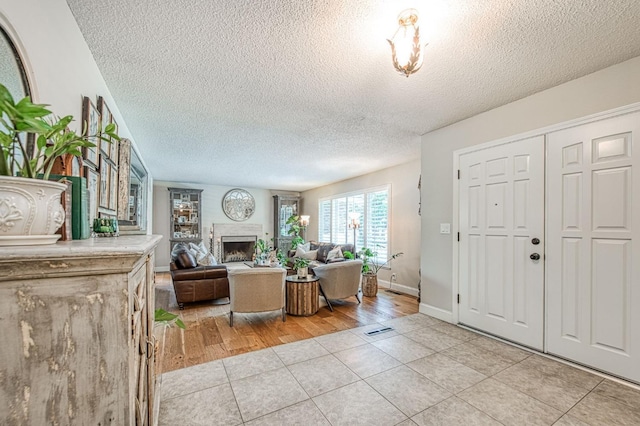 foyer featuring a textured ceiling, baseboards, light tile patterned floors, and a fireplace