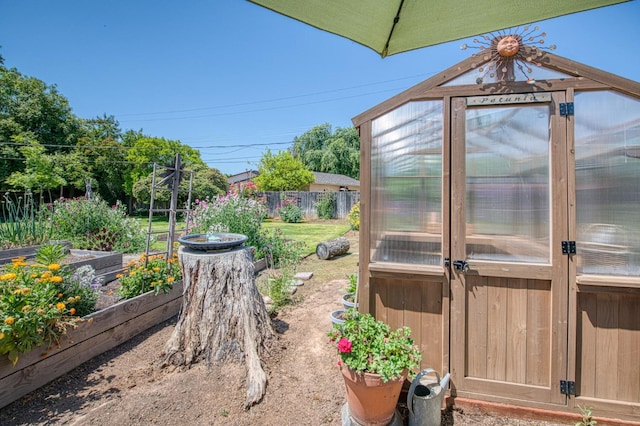 view of yard featuring a vegetable garden, fence, a greenhouse, and an outdoor structure
