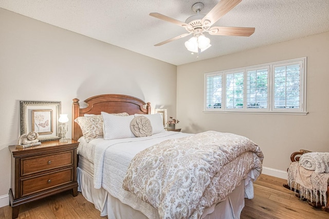 bedroom featuring baseboards, ceiling fan, a textured ceiling, and wood finished floors
