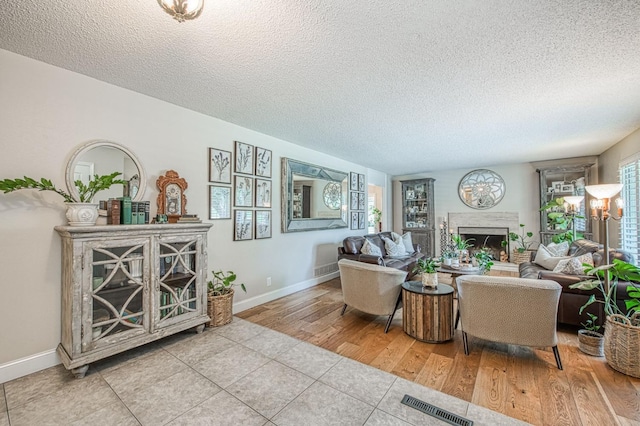 tiled living area with a textured ceiling, visible vents, a fireplace, and baseboards