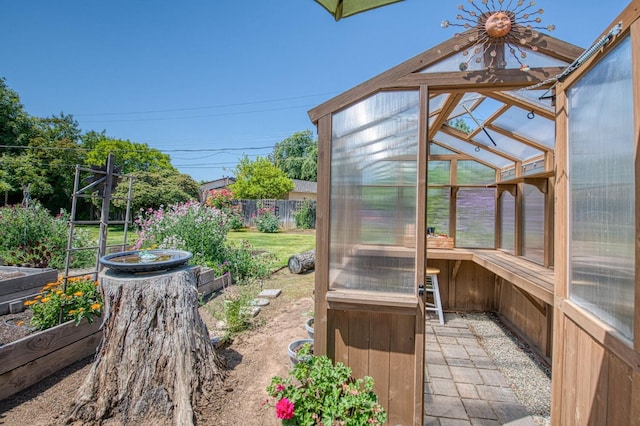 view of yard featuring a greenhouse, an outdoor structure, fence, and a vegetable garden