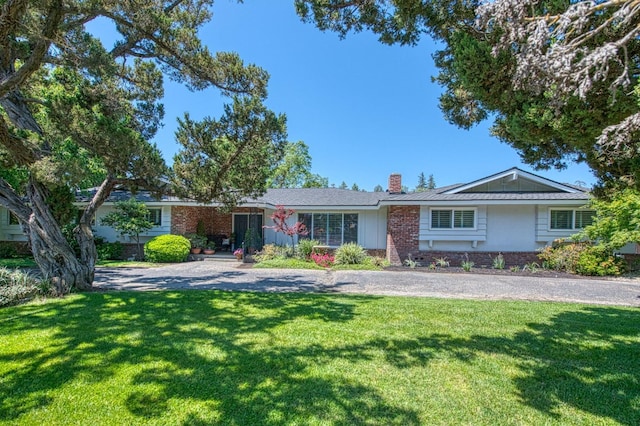 single story home featuring a chimney, brick siding, and a front yard