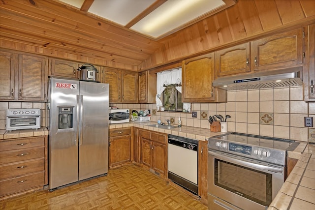 39090 Woodland Rd, Shaver Lake, CA 93664 - kitchen featuring stainless steel appliances, tile counters, under cabinet range hood, tasteful backsplash, and vaulted ceiling