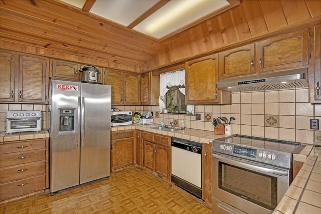 39090 Woodland Rd, Shaver Lake, CA 93664 - kitchen featuring stainless steel appliances, tile counters, under cabinet range hood, tasteful backsplash, and vaulted ceiling