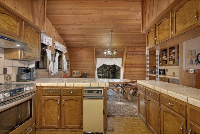 39090 Woodland Rd, Shaver Lake, CA 93664 - kitchen with stainless steel electric range oven, a peninsula, a chandelier, brown cabinets, and wood walls