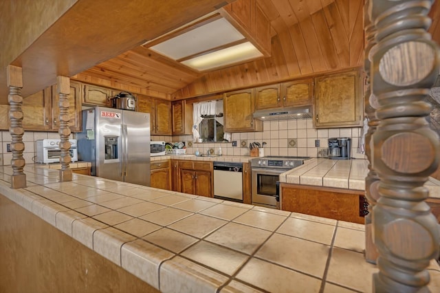 39090 Woodland Rd, Shaver Lake, CA 93664 - kitchen featuring stainless steel appliances, under cabinet range hood, tasteful backsplash, brown cabinetry, and tile counters