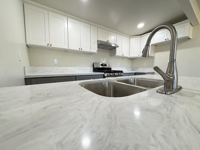 kitchen featuring stainless steel gas range oven, recessed lighting, under cabinet range hood, white cabinetry, and light stone countertops