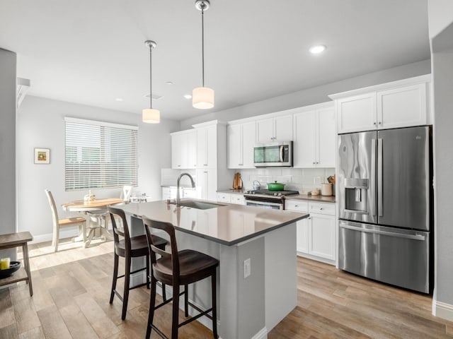 kitchen with appliances with stainless steel finishes, light wood-style flooring, an island with sink, and a sink