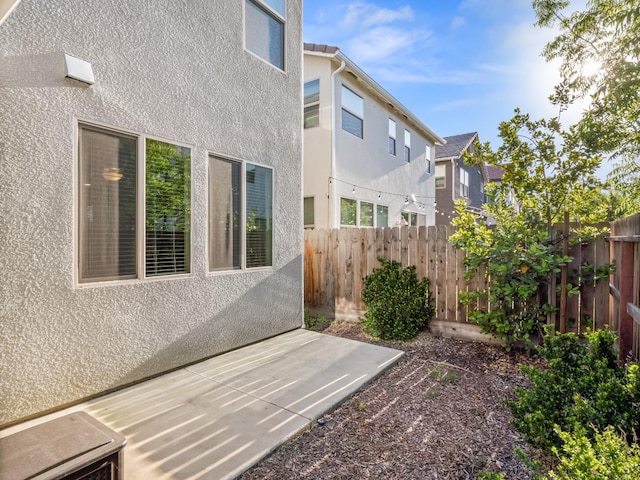 view of side of property with fence, a patio, stucco siding, and a residential view