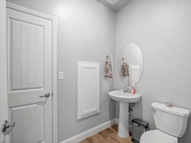 half bathroom with toilet, wood finished floors, and baseboards