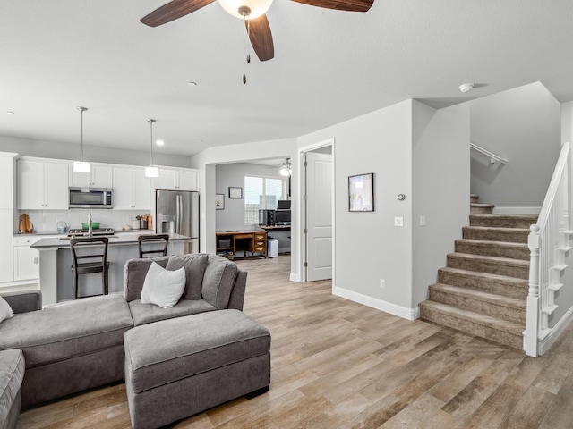 living room with stairway, light wood-style flooring, baseboards, and a ceiling fan