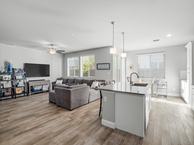 kitchen with visible vents, a sink, a center island with sink, white cabinets, and light wood-type flooring