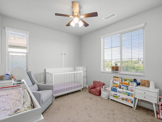 carpeted bedroom with ceiling fan, a nursery area, and visible vents