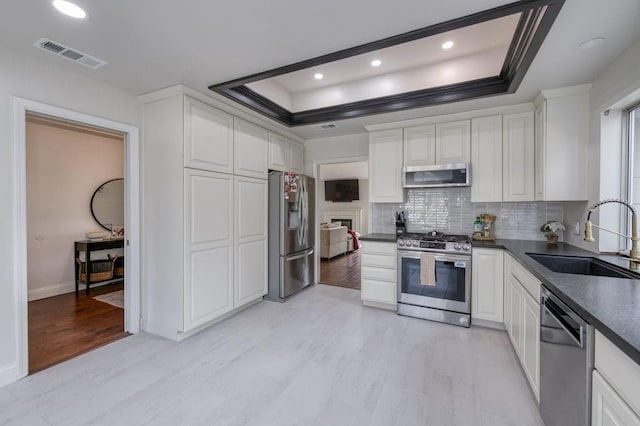 kitchen featuring a tray ceiling, visible vents, a sink, dark countertops, and appliances with stainless steel finishes