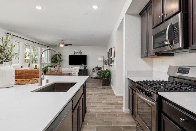 kitchen featuring a sink, stainless steel appliances, light countertops, a ceiling fan, and dark brown cabinets