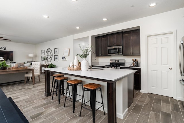 kitchen featuring a breakfast bar, a sink, stainless steel appliances, wood tiled floor, and open floor plan