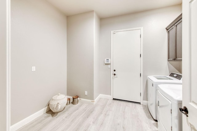 laundry room featuring cabinet space, washing machine and dryer, light wood-style flooring, and baseboards